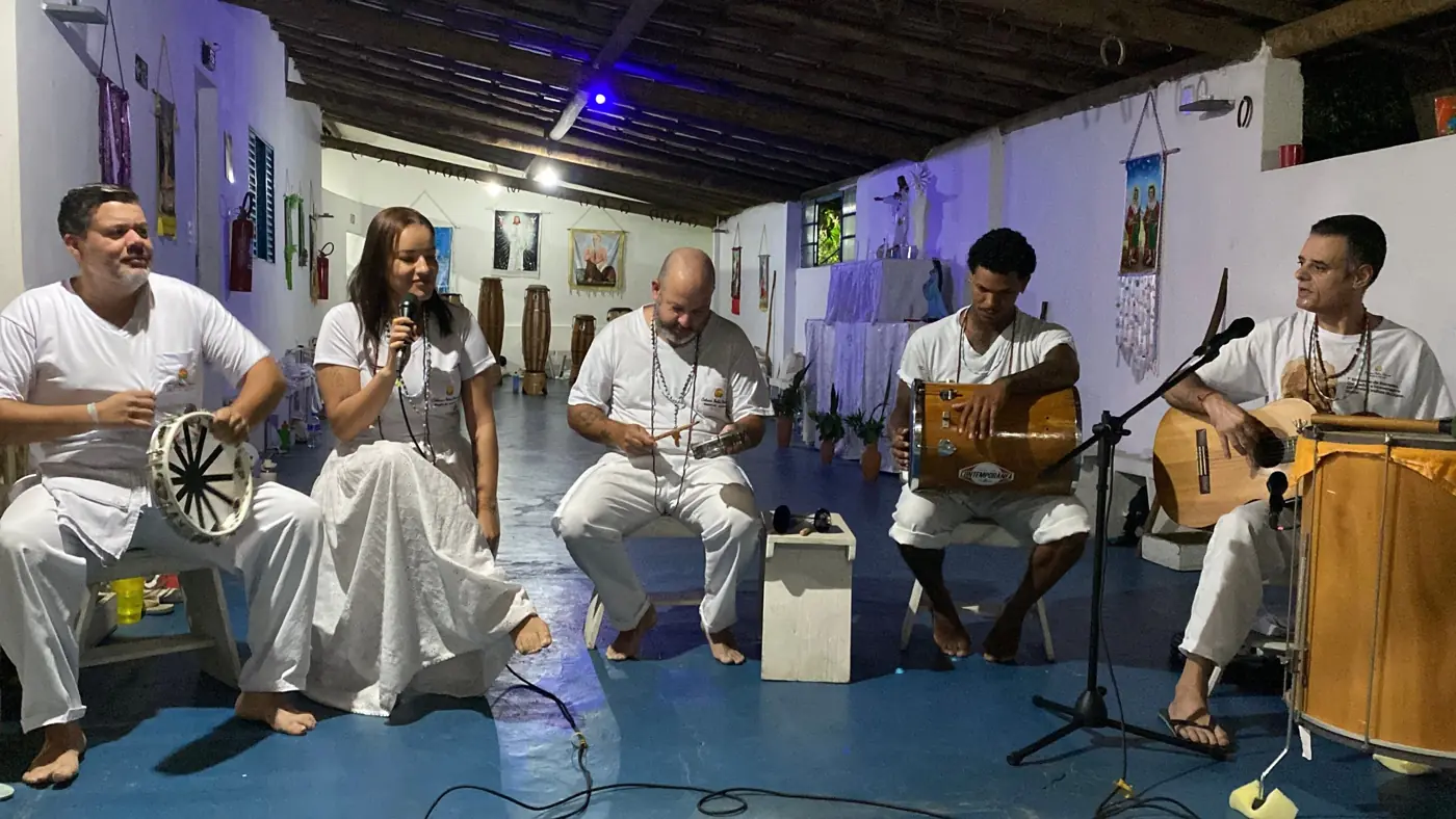 Integrantes do Encantuá, vestidos de branco, tocando pandeiro, tamborim, repique, violão e surdo na sede da Cabana