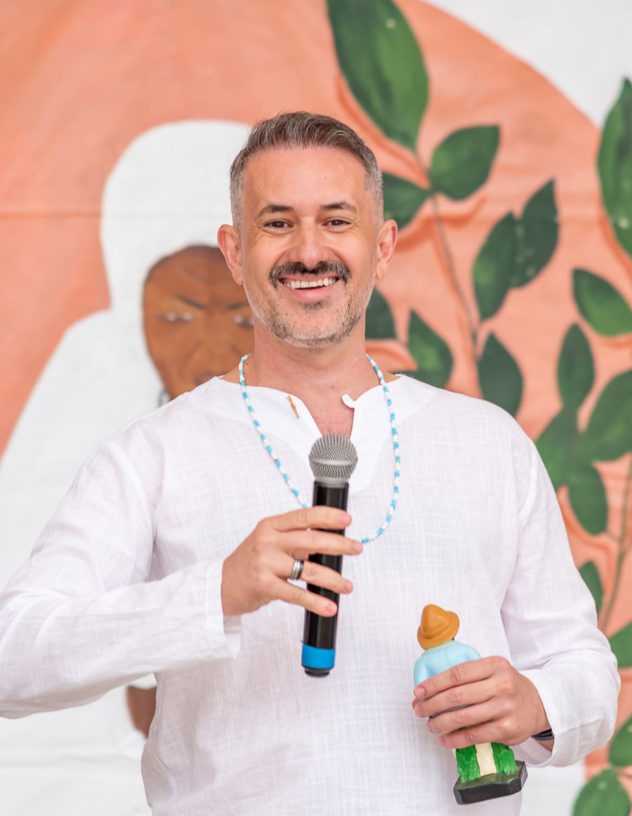 Pai Erlon de Oxalá, vestido de branco, sorrindo e segurando um microfone